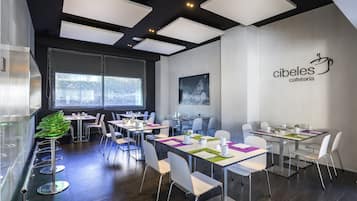 Un café moderno con varias mesas y sillas, un ventanal grande e iluminación empotrada en el techo.