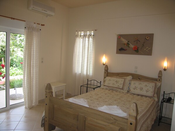 A bedroom with a wooden bed, a small bedside table, a wall-mounted light, and a window with curtains. - New Kydonia Suites & Studios (Chania)