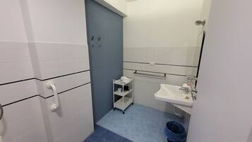 A bathroom with white tiled walls, a blue floor, a white sink, a mirror, a towel rack, and a trash bin.