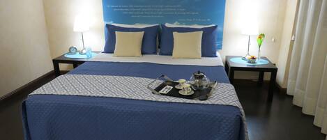 A hotel room with a large bed, two bedside tables, a nightstand, a tray with tea set, and a poster on the wall.