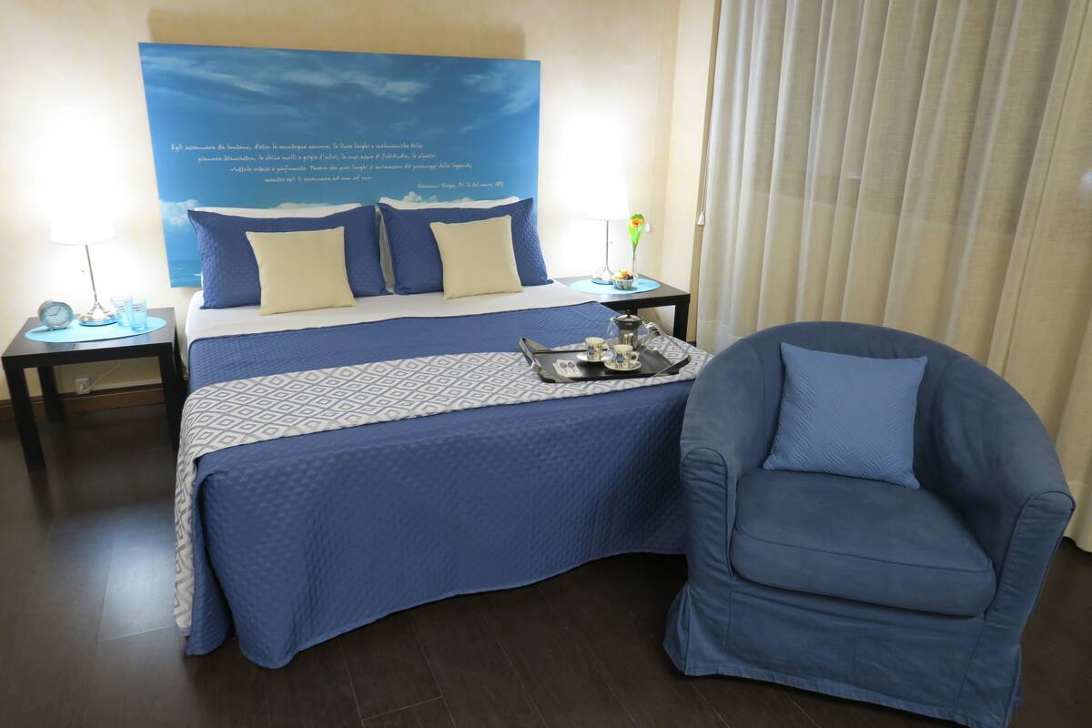 A hotel room with a bed, a chair, a nightstand, a lamp, and a poster on the wall.