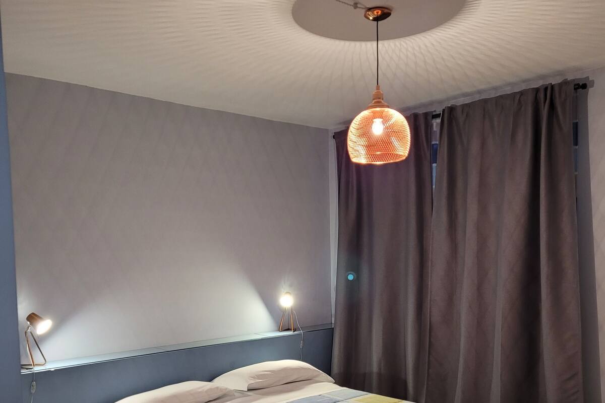A bedroom with two beds, a ceiling light fixture, and a window with curtains.