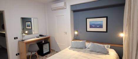 A bedroom with a bed, desk, chair, and an air conditioning unit.