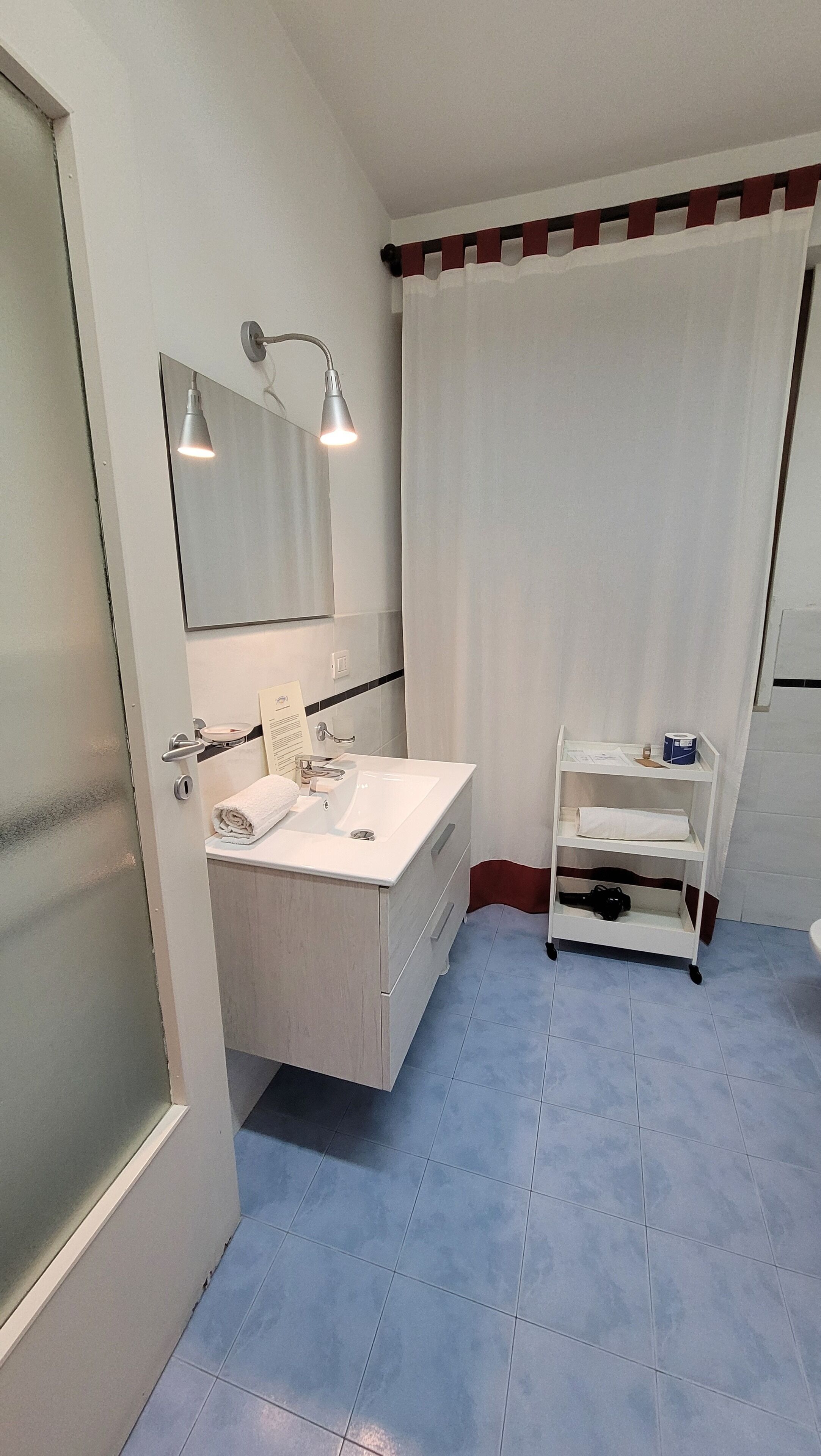 Ein modernes Badezimmer mit einem weißen Waschtisch, einem Spiegel, einem Waschbecken und einer Duschvorhang.