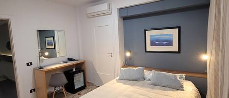 Una habitación de hotel con cama, escritorio, silla y un cuadro en la pared.