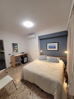 Una habitación de hotel con cama, escritorio, silla y un cuadro en la pared.
