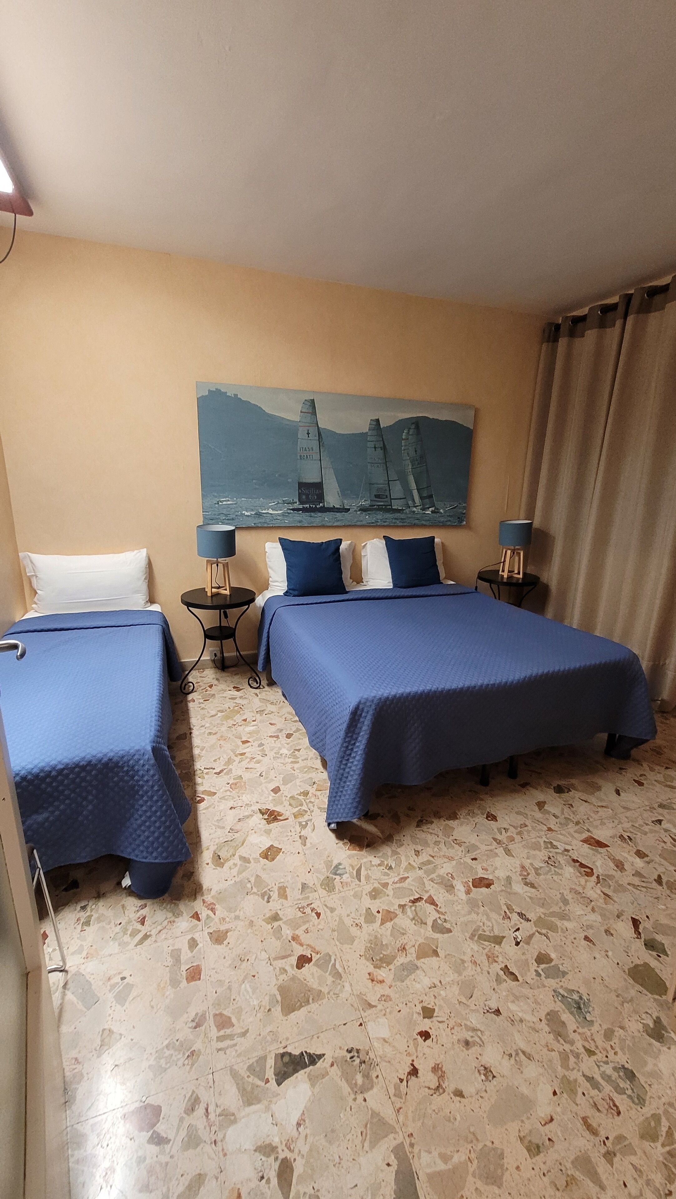 A hotel room with two beds, a painting of sailboats on the wall, and a tiled floor.