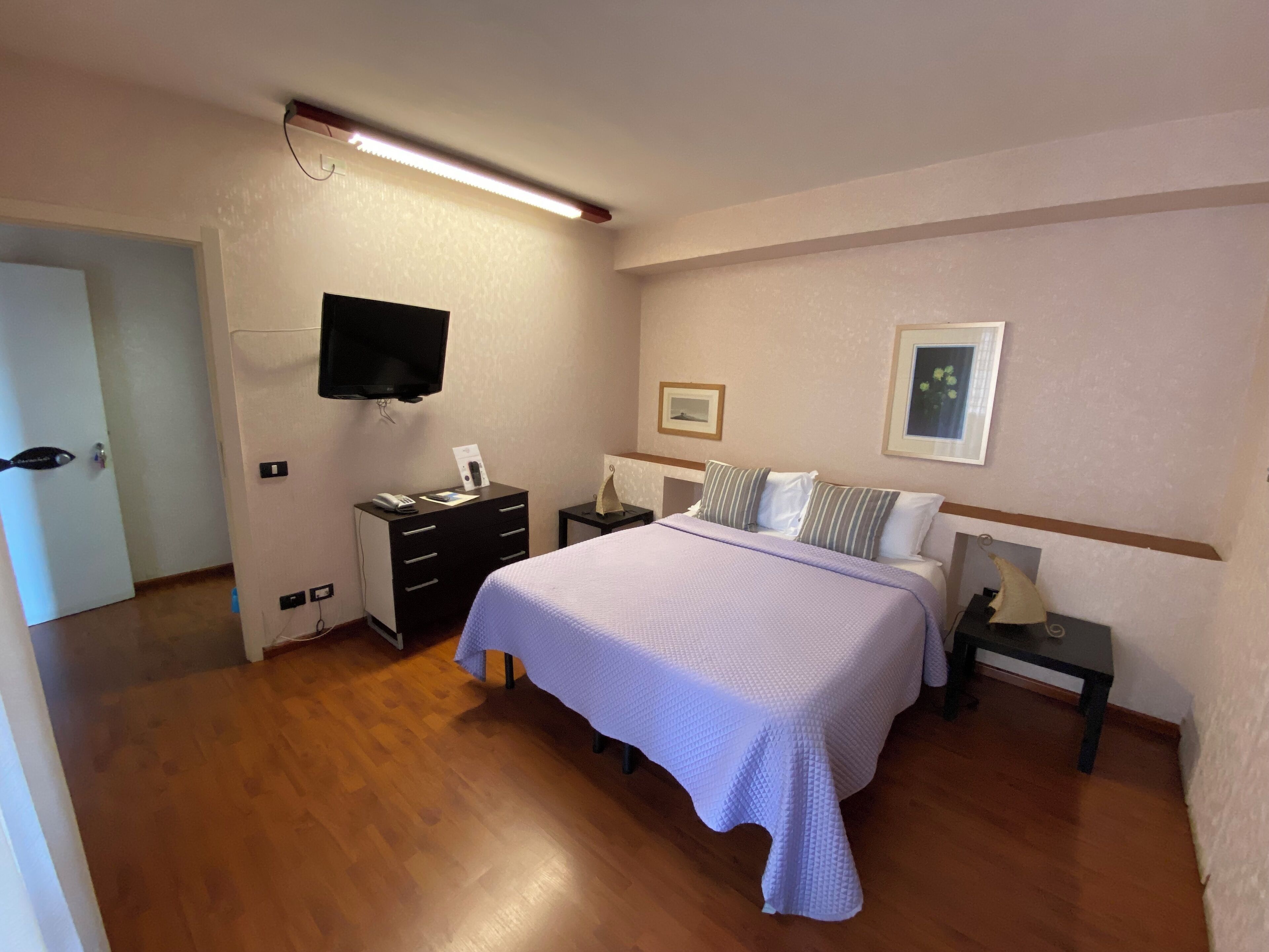 Quarto de hotel com uma cama, mesas de cabeceira, uma TV de tela plana e quadros nas paredes.