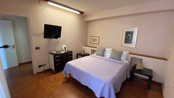 Quarto de hotel com uma cama, mesas de cabeceira, uma TV de tela plana e quadros nas paredes.