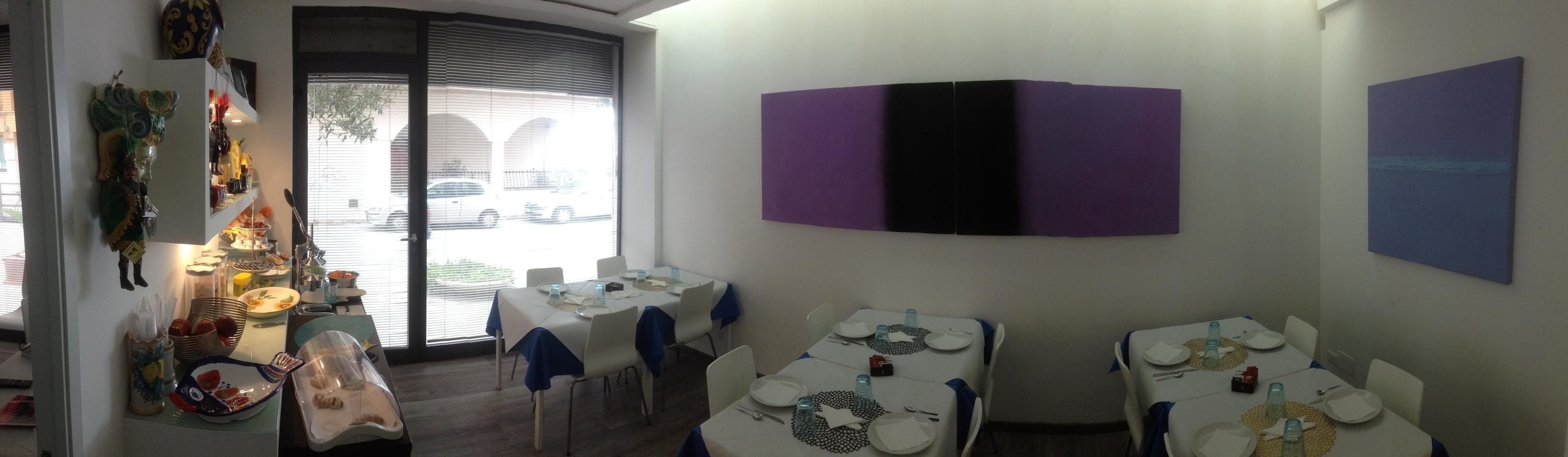 Un comedor con mesas dispuestas para el servicio, un ventanal con persianas y obras de arte colgadas en la pared.
