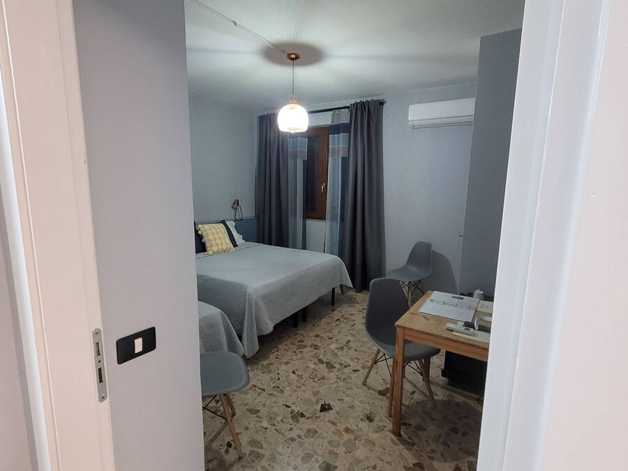A room with two beds, a desk, and a chair. There is a ceiling light and a window with curtains.