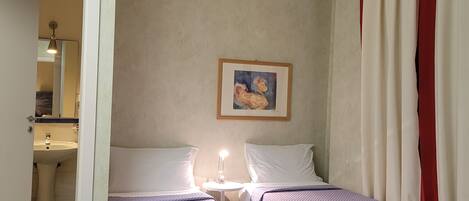 A room with two beds, a painting on the wall, and a bathroom visible through an open door.