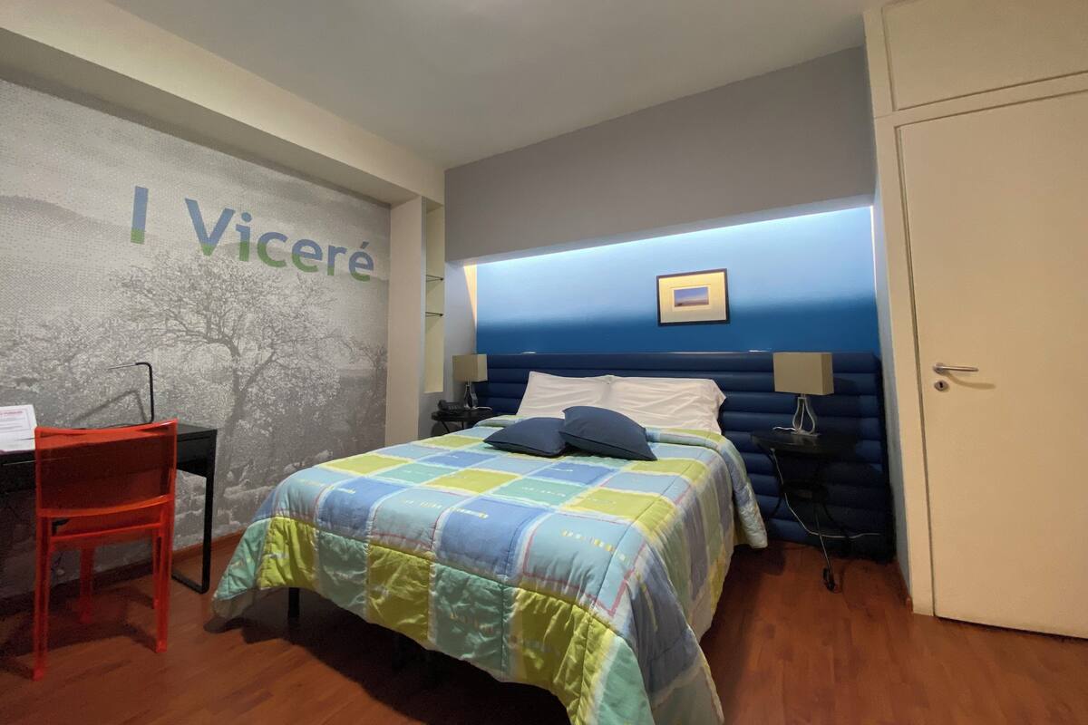 A hotel room with a bed, a desk, a chair, and a wardrobe.