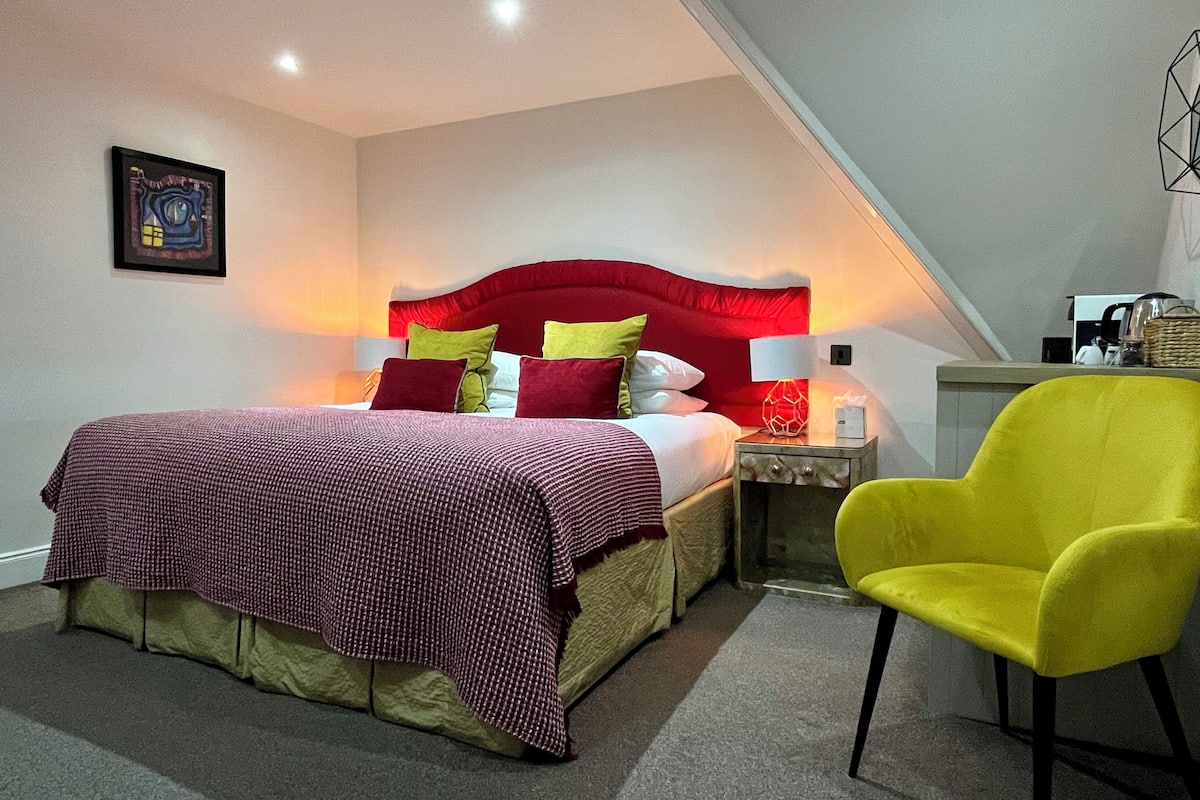 A hotel room with a bed, a nightstand, a chair, and a wall-mounted artwork.