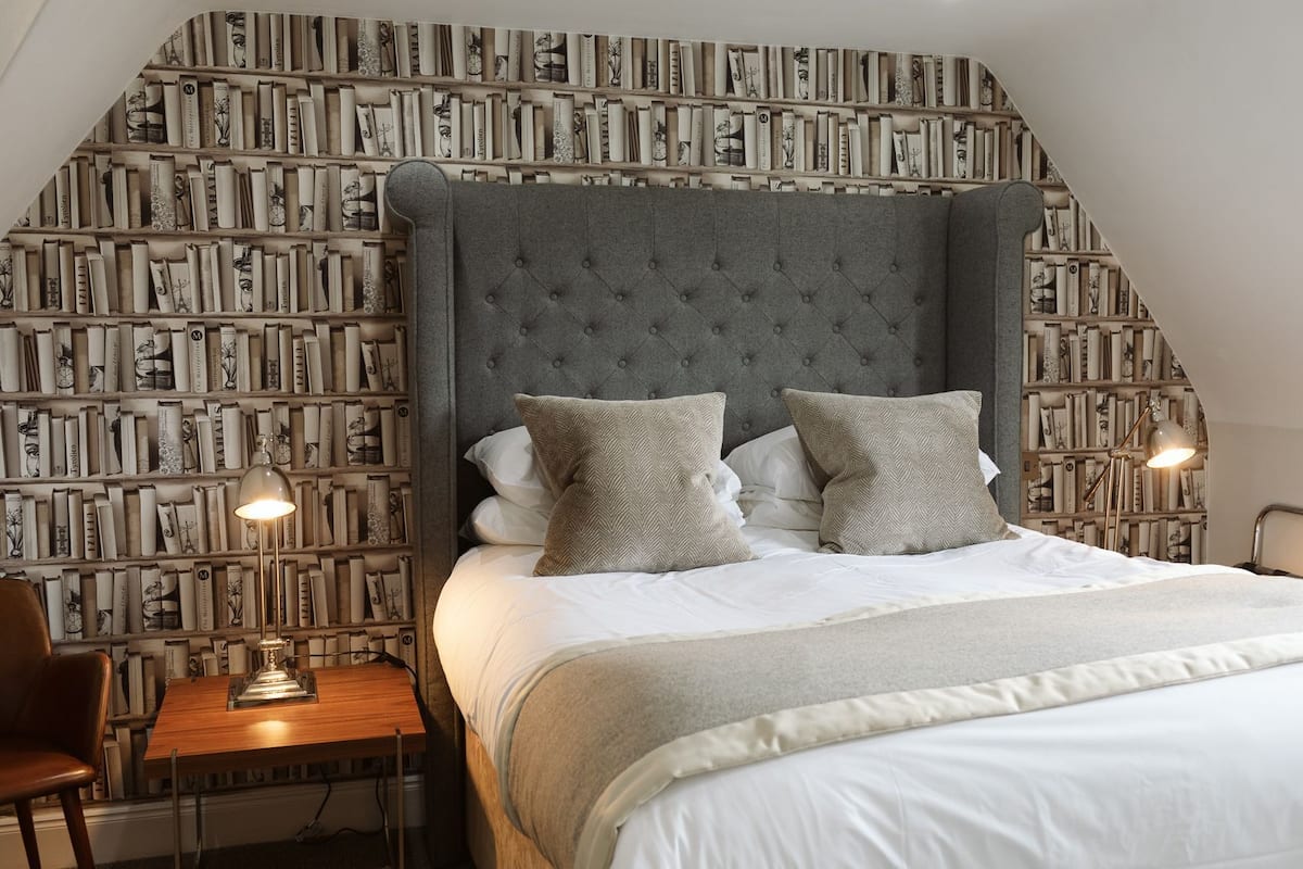 A bedroom with a large bed, a bookshelf wall, and a desk with a lamp.