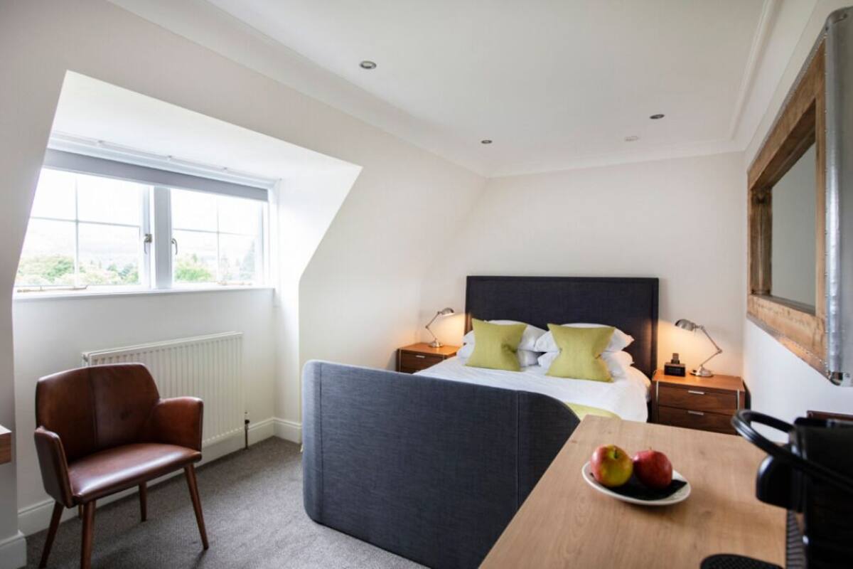 A bedroom with a bed, bedside tables, a chair, a table with fruit, and a window.