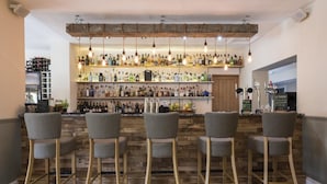Zona de bar amb sòl de fusta, tamborets grisos i diverses ampolles a les prestatgeries.