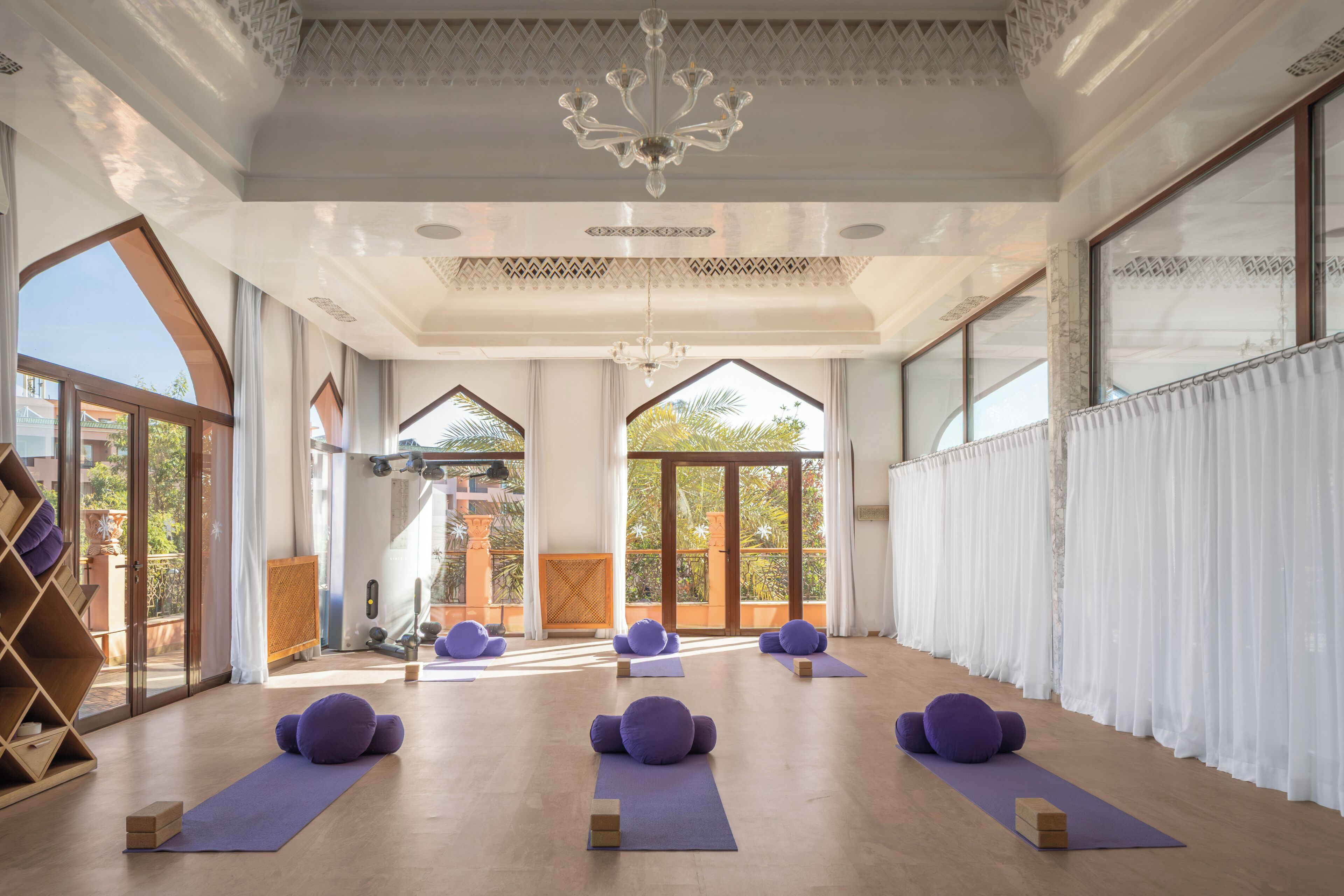 A spacious room with large windows, a wooden floor, and purple exercise mats.