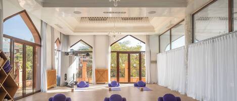 A spacious room with large windows, a wooden floor, and purple exercise mats.