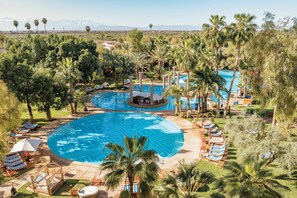 A large outdoor swimming pool surrounded by palm trees and lounge chairs, with a view of mountains in the background. - Es Saadi Marrakech Resort Palace (Marrakech)