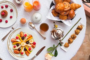 A breakfast setting with croissants, fruit, pastries, and a teapot on a table. - Es Saadi Marrakech Resort Palace (Marrakech)