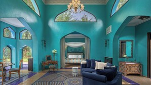 Quarto em tons de turquesa com cama de dossel, um lustre e vista para o exterior através de janelas em arco.