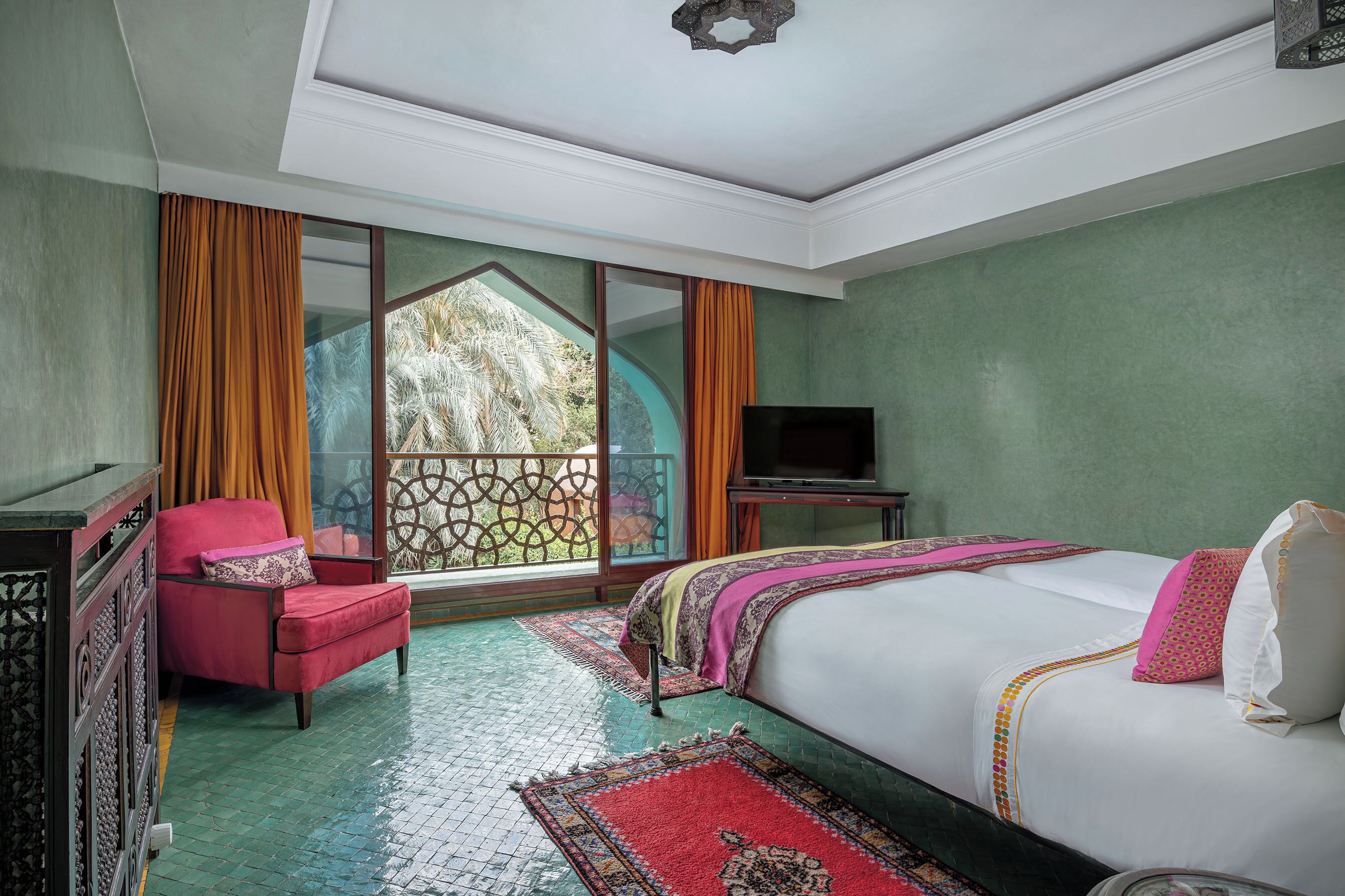 A hotel room with a bed, a chair, a TV, and a balcony with curtains.