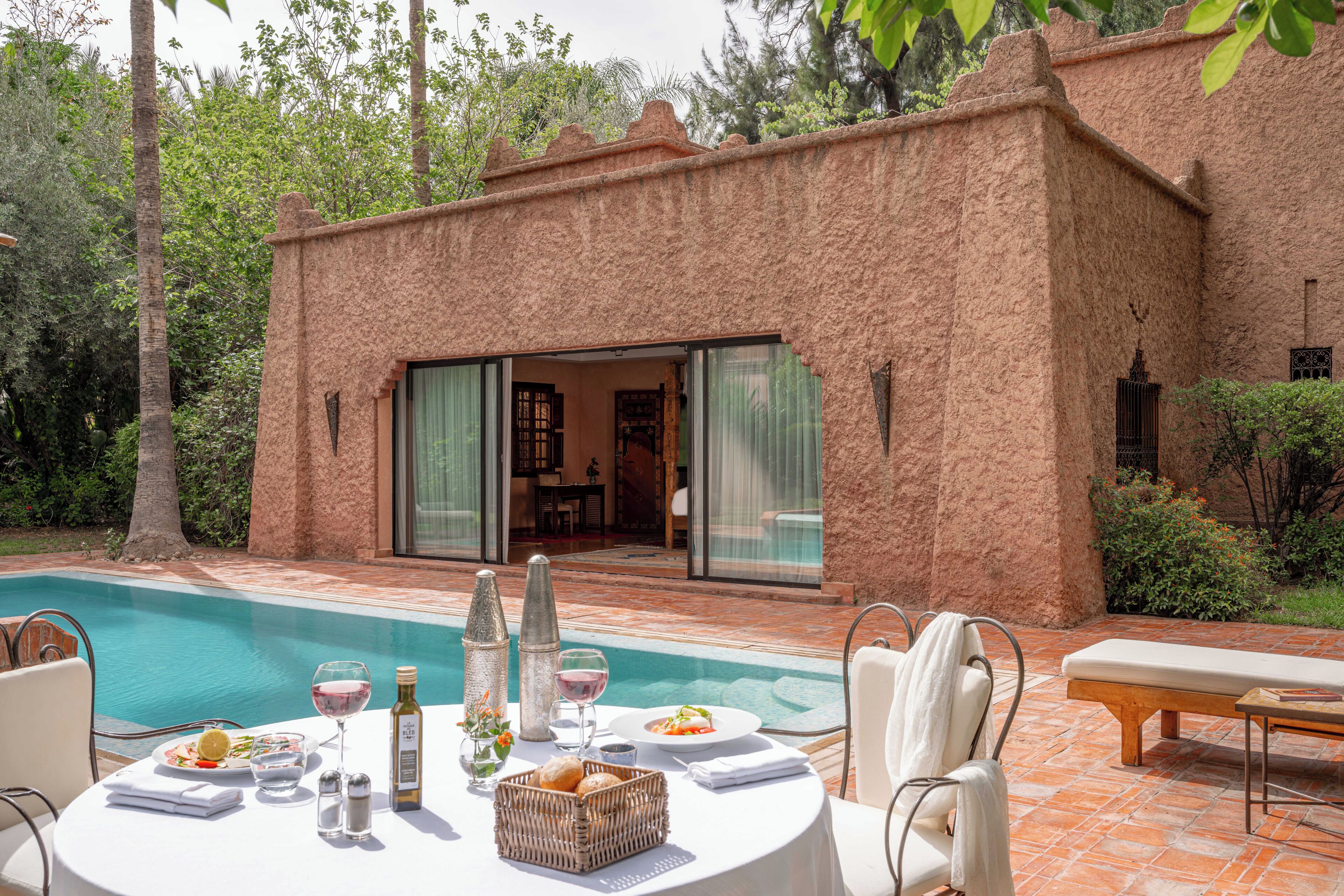 A poolside dining area with a table set for two, a glass of wine, and a basket of bread.