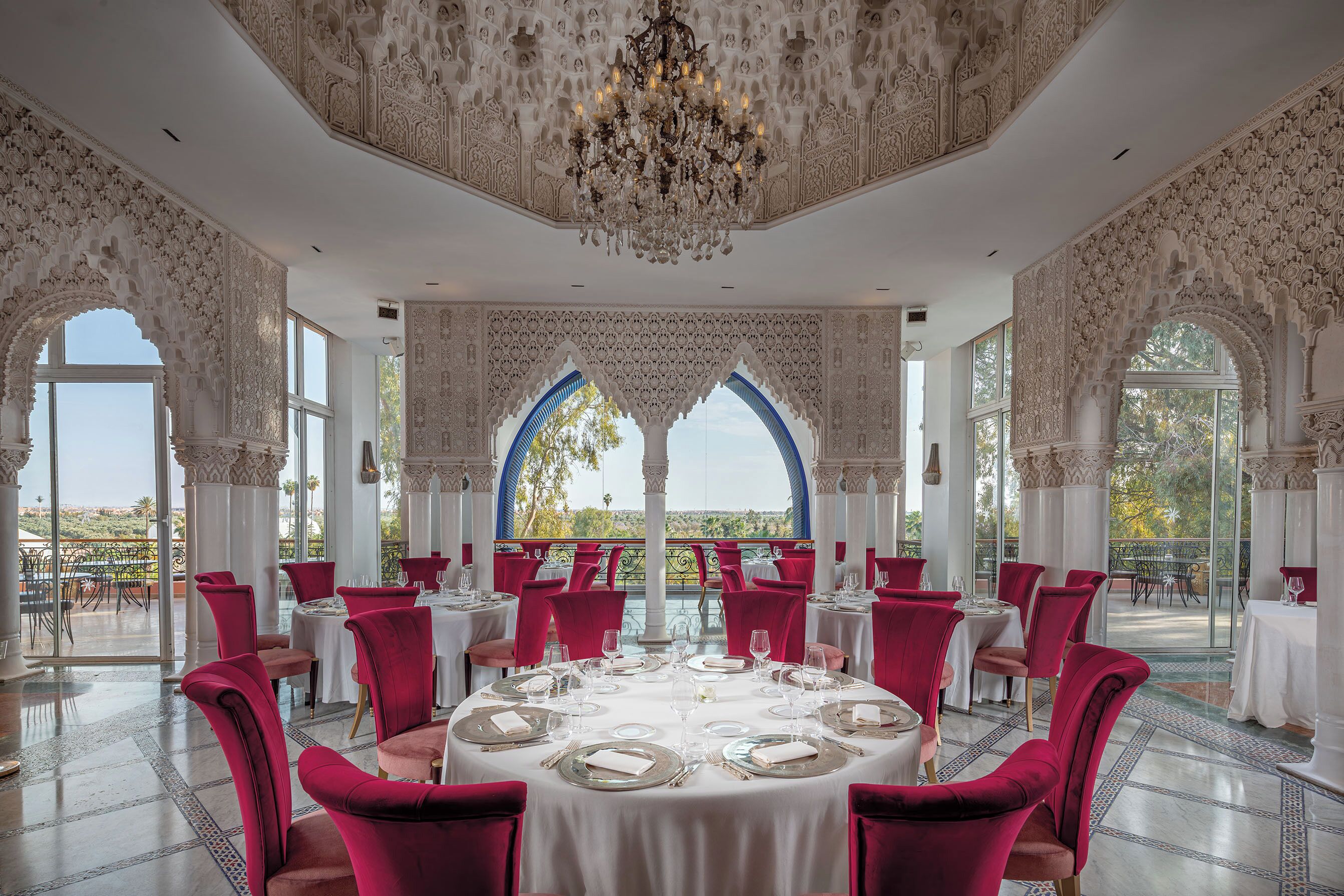 A dining area with ornate ceiling and arches, tables set for a meal, and a view of the outdoors.