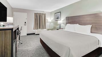 A hotel room with a large bed, a desk with a lamp, a chair, a wardrobe, and a window with curtains.