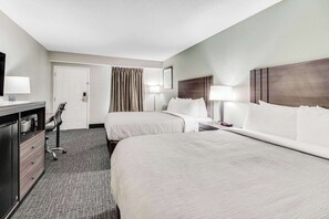 A hotel room with two beds, a desk, a chair, and a door.