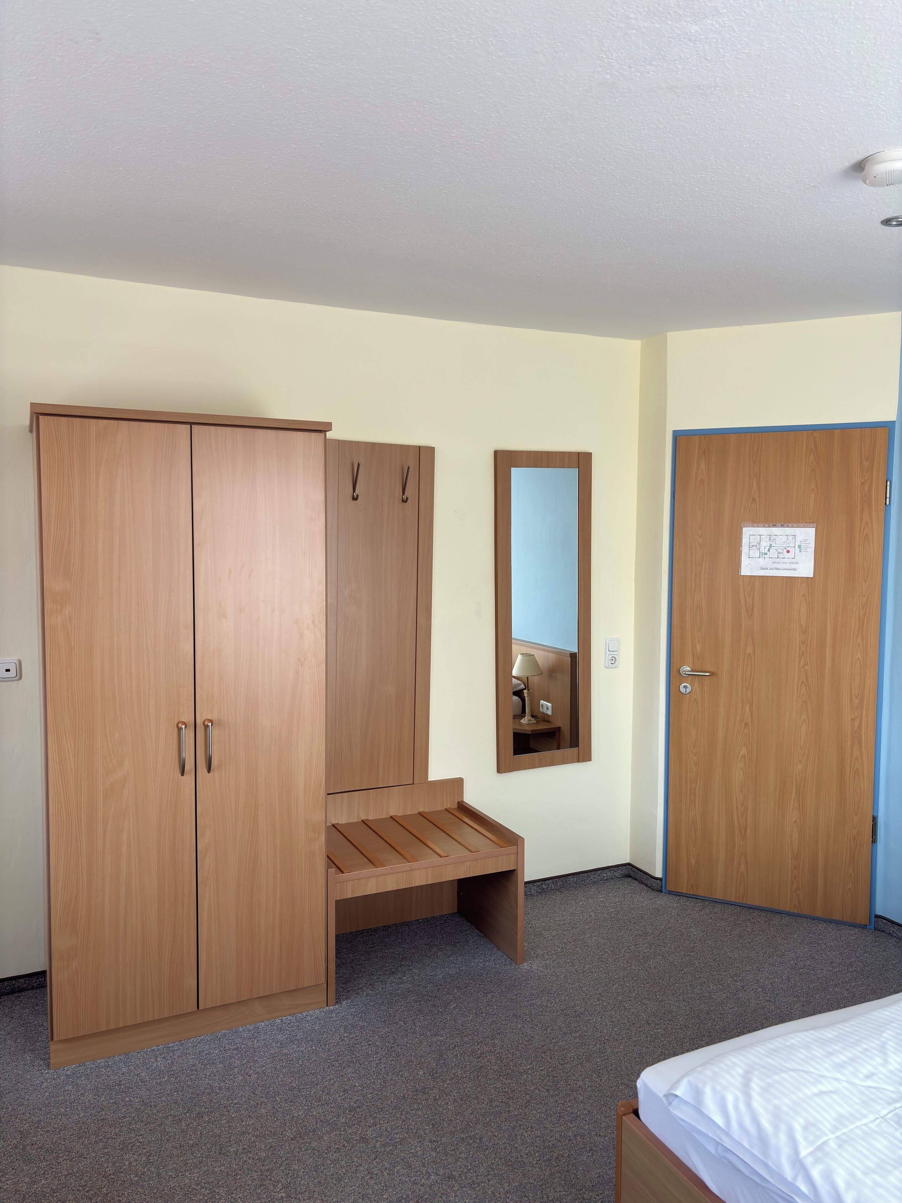 Un dormitorio con cama, armario, espejo y una puerta con un cartel.