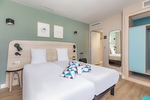 Una habitación de hotel moderna con una cama grande, una mesita de noche, un espejo y un armario.