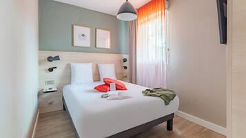 A neatly made bed with pillows, a bedside table with a lamp, and a window with curtains.