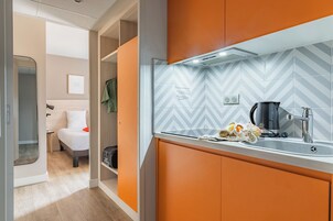 Habitación de hotel compacta con kitchenette, una cama con ropa de cama blanca y vista al baño contiguo.
