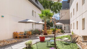 An outdoor patio area with seating, umbrellas, and a small garden. - Appart'City Confort Montpellier Gare Saint Roch (Montpellier)