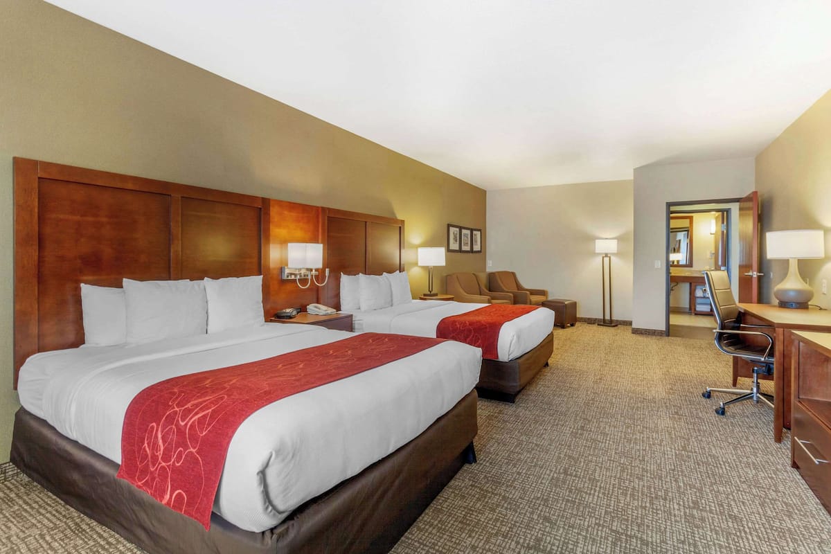 A hotel room with two beds, a desk, a chair, and a lamp.