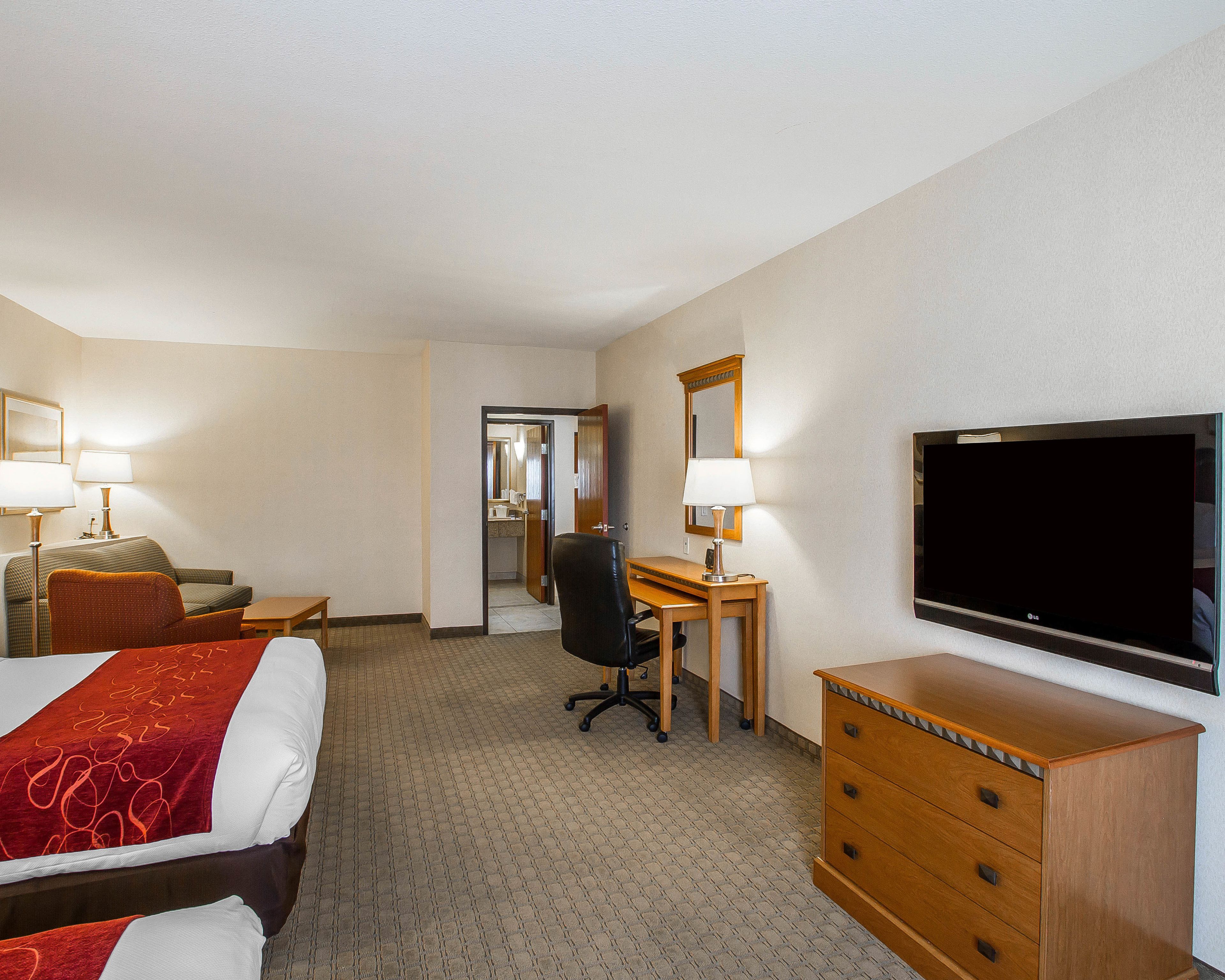 Hotelkamer met een bed, bureau, stoel, kaptafel, televisie en een badkamer zichtbaar door een geopende deur.