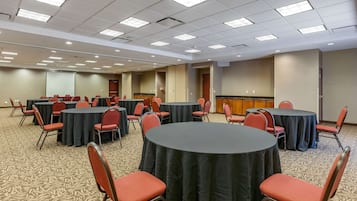 A conference room with multiple tables and chairs, carpeted floor, and ceiling lights.