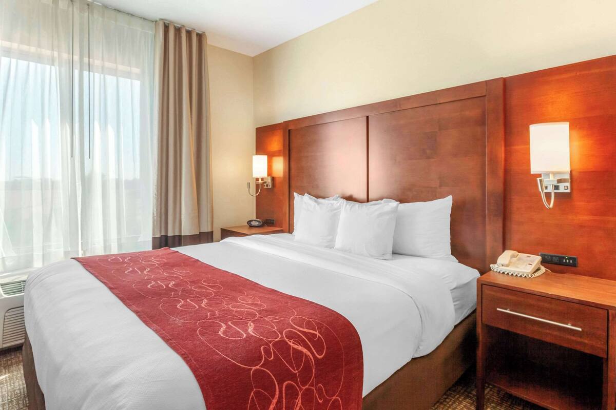 A hotel room with a large bed, a wooden headboard, a bedside table with a lamp, and a telephone.