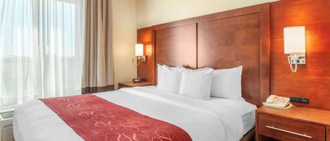 Una habitación de hotel con una cama grande, cabecera de madera, mesita de noche con lámpara y teléfono.