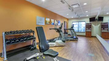 Ein Fitnessstudio mit Trainingsgeräten, darunter Kurzhanteln, eine Bank, Laufbänder und eine Wand mit Motivationspostern.