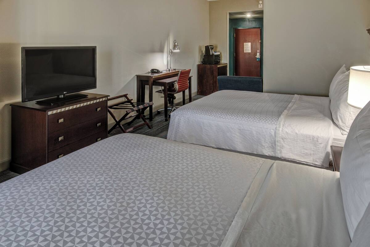 A hotel room with two beds, a desk with a chair, a television, and a coffee machine.