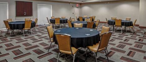 A conference room with multiple tables and chairs, carpeted floor, and a projector on the ceiling.