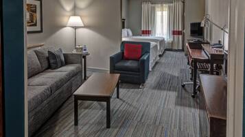 Een hotelkamer met een bank, fauteuil, een klein tafeltje en een bed met gordijnen.
