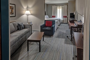 A hotel room with a sofa, armchair, small table, and a bed with curtains. - Four Points by Sheraton Memphis Southwind (Memphis)