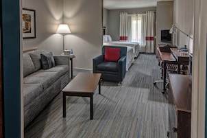Habitación de hotel con sofá, sillón, mesita y cama con cortinas.