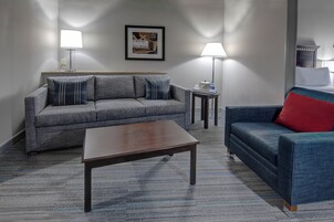 A living room with a grey sofa, a blue sofa with a red pillow, a wooden coffee table, and two floor lamps.