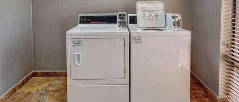 Une buanderie équipée de deux machines à laver et deux sèche-linge superposés, d’un panneau de commande et d’une fenêtre avec des stores.