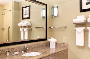 A bathroom with a granite countertop, a sink, a mirror, a framed picture, and a towel rack with folded towels.